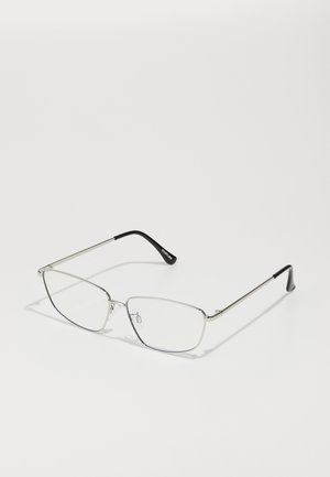 Occhiali in metallo con una sottile montatura argentata, lenti angolari, vetro trasparente e accenti in gomma nera sulle punte delle stanghette. Design leggero e minimal.