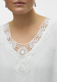 Hvid top med detaljeret hæklede blonder omkring halsudskæringen, med struktureret stof og en afslappet pasform.