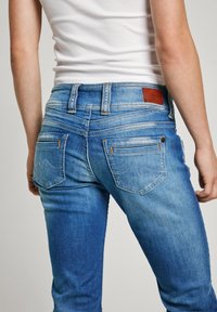 Blå denimjeans med slim fit, kontrastsömmar, läderlogotyp och en distinkt bakfickdesign med böjda sömmar.