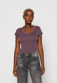 Fialové tričko s výstřihem do V vyrobené z měkké látky, s krátkými rukávy a slim fit střihem, v kombinaci s vysokým pasem a vybledlými černými džíny.