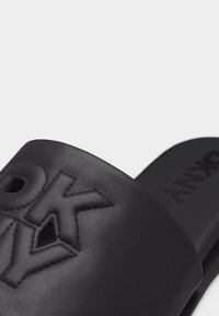 Sandale à glissière noire avec le logo PXNY en relief sur la bride et la marque PXNY sur la semelle intérieure en gros plan.