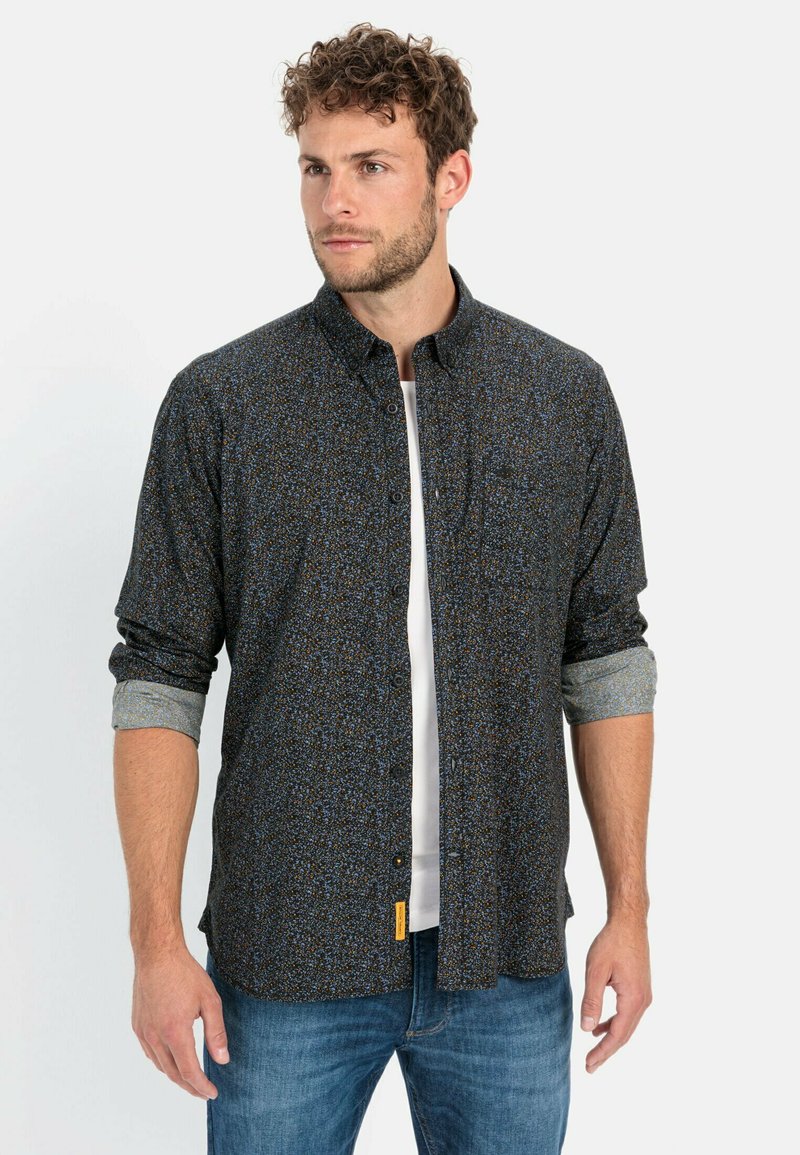 Sort skjorte med knaplukning i en flerfarvet prikket mønster, lange ærmer og en kontrastfarvet indre mansjettdetalje, parret med blå jeans.