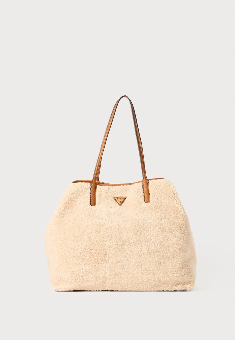 Sac cabas beige à texture douce avec des poignées en cuir marron et un petit logo triangulaire au centre devant sur un fond uni.