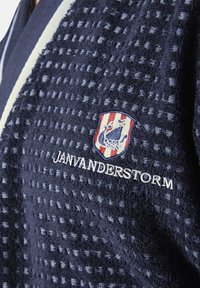 Navy blue textured bathrobe with a grid pattern, featuring a shield logo and embroidered "JANVANDERSTORM" in white.