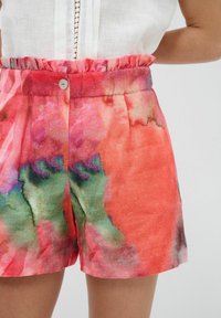 Pantalones cortos coloridos y ligeros con un patrón de acuarela en tonos de rojo, verde y púrpura, con una cinturilla elástica fruncida y un detalle de botón.