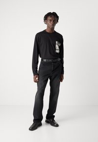 Zwarte langemouwhemd met getextureerde zak, gecombineerd met donkergrijze straight-leg jeans en zwarte schoenen. Eenvoudig ontwerp, minimale accenten.