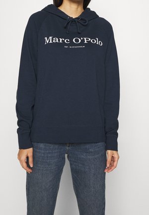 Sudadera con capucha de color azul marino con cordón, que presenta el texto impreso en blanco "Marc O'Polo" y "EST. EN ESTOCOLMO." Tejido suave, corte relajado.