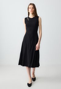 Schwarzes ärmelloses Kleid mit eng anliegendem Oberteil und weit ausgestellt Rock. Verfügt über ein dezentes asymmetrisches Ausschnittdetail. Glatte Stofftextur.