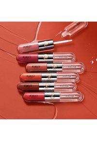 Zes KIKO Milano lipglossbuisjes in verschillende tinten roze, rood, oranje en bruin op een bijpassende glanzende oranje achtergrond. Eén applicator zichtbaar.
