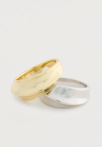 Dve hladké, leštené prstene uložené na sebe - jeden zlatý, jeden strieborný - na obyčajnom bielom pozadí.