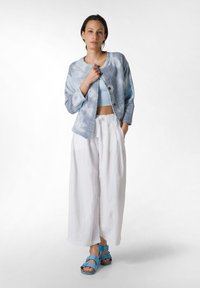 Giacca azzurro chiaro, strutturata, con scollo rotondo e bottoni, abbinata a pantaloni bianchi a gamba larga e sandali blu con cinturini.