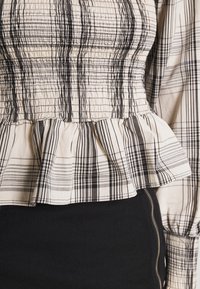 Mustavalkoinen ruudullinen pusero, jossa on smokkikangasta, peplum-helma ja pitkät hihat, joissa on poimuttamista. Materiaali näyttää kevyeltä.