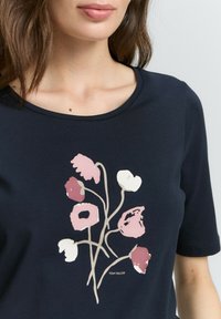 Marineblaues T-Shirt mit floralem Grafikdesign in Pink und Weiß. Weicher Stoff mit Rundhalsausschnitt und kurzen Ärmeln. Marke: TOM TAILOR.