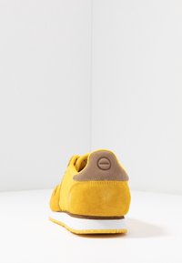 Gelbe Wildledersneaker mit einer beigefarbenen Stofffersenlasche. Verfügt über eine weiße Zwischensohle und eine strukturierte Gummisohle. Rundes Logo an der Ferse.
