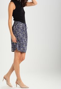 Marinblå kjol med paisleymönster, elastisk midja och dragsko. Kombinerad med en figursydd svart ärmlös topp och neutrala klackar.