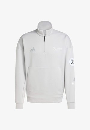 Biała bluza z półzamkiem i kolarzem, przednia kieszeń oraz haftowane logo. Posiada szare akcenty i trzy paski na rękawach.