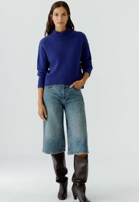 Garen gebreide coltrui in diepblauw, gecombineerd met lichtblauwe wijde jeans en bruin leren laarzen tot de knie met hakken. Stevige textuur, casual ontwerp.