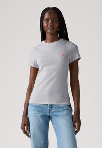 Grå bomulds t-shirt med korte ærmer, rund halsudskæring og et lille rødt Levi's logo på venstre bryst. Båret med lyseblå jeans.
