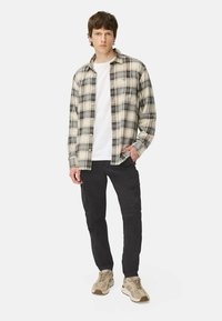 Rutet flanellskjorte i beige, blå og mørkegrøn, lagd over en hvid t-shirt. Sorte cargo bukser og lysebrune sneakers.