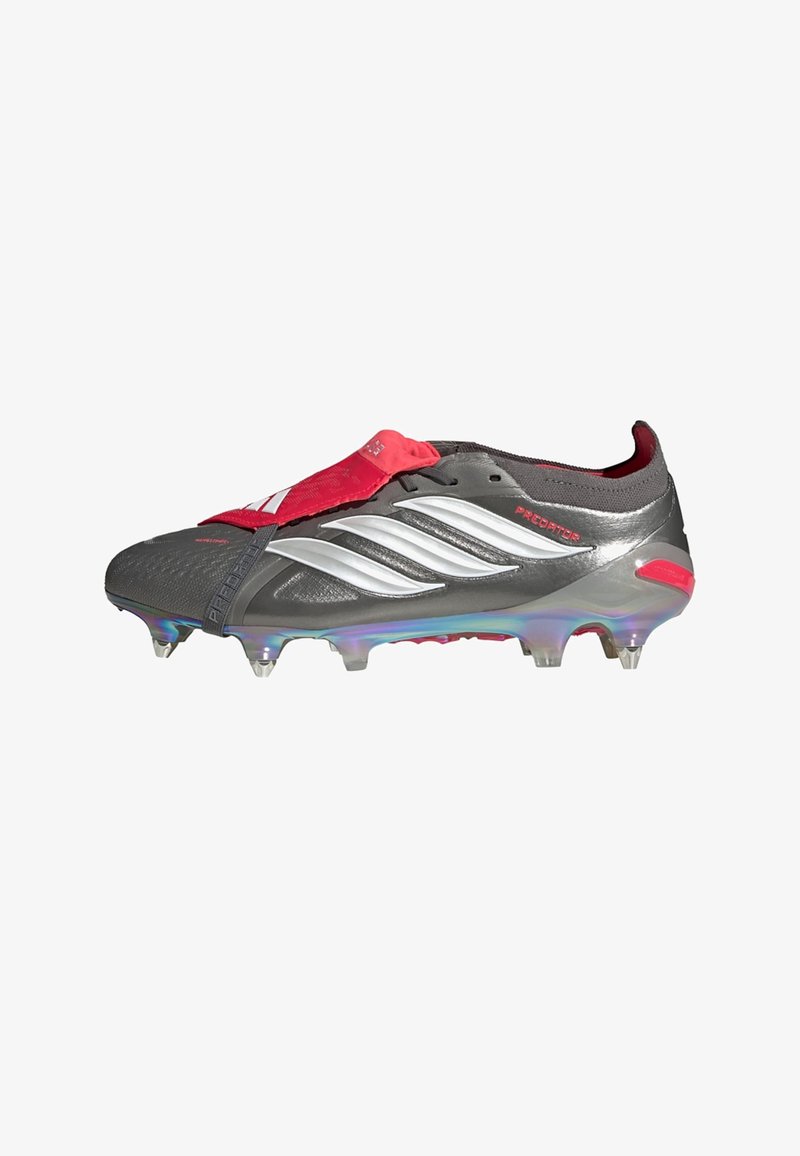 Bota de fútbol gris con una tira roja, detalles plateados y una superficie texturizada. Tachones transparentes en la suela proporcionan tracción.