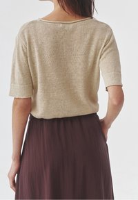 Jersey beige de punto con mangas cortas, ajuste relajado y escote amplio, combinado con una falda suelta de color marrón oscuro.