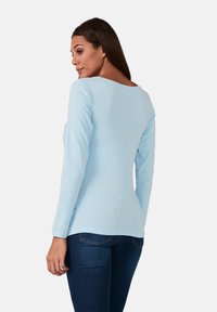 Hellblaues Langarmoberteil mit rundem Halsausschnitt und schmaler Passform, aus weichem Stoff gefertigt, kombiniert mit dunkelblauen Jeans.