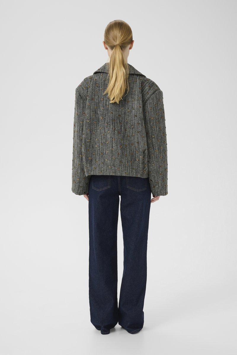 Grå herringbone tweedjakke med en bred klap, rundede skuldre og en boxy pasform, parret med mørkeblå vidde denimjeans.