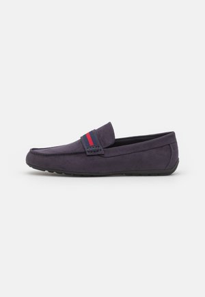 Mocassins en daim bleu marine pour homme avec un détail en tissu rayé rouge et bleu sur la sangle, semelle en caoutchouc noir et couture le long des bords.
