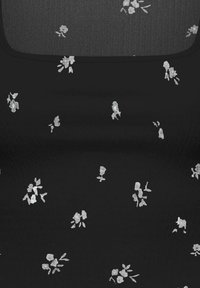 Tissu noir avec de petits bouquets floraux blancs éparpillés et un col carré avec un panneau contrastant.