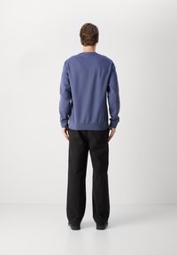 Lila sweatshirt med långa ärmar och ribbade muddar, parat med svarta, löst sittande byxor. Slät tygtextur, enkel design.