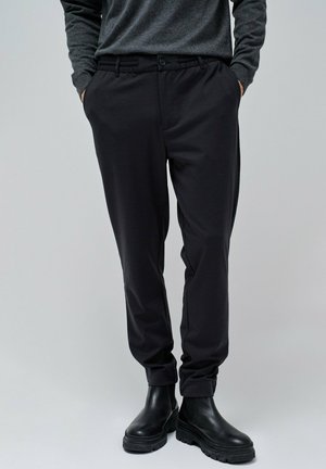 Pantalones negros ajustados con una textura suave, con cierre de botón y bolsillos laterales, combinados con botas de tobillo negras.