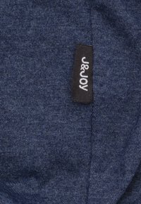 Marineblauwe stof met een gestructureerde brei. Zichtbaar etiket met "J&JOY" in het wit op een zwarte achtergrond, waarop stik- en materiaaldetails te zien zijn.