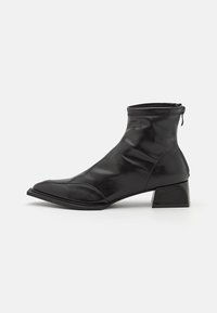 Bottes chevilles en cuir noir avec une finition brillante, dotées d'un bout pointu, d'un petit talon bloc et d'une fermeture éclair à l'arrière.