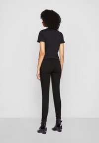 Camiseta ajustada negra de manga corta, combinada con jeans negros ajustados. La modelo lleva botas negras hasta el tobillo. Tejido suave con detalles mínimos.