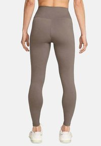 Leggings marron taille haute en matériau extensible, design ajusté, texture lisse et construction sans coutures, associés à des baskets blanches.