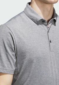 Szara koszulka polo z teksturowanym wzorem, krótkimi rękawami i kołnierzykiem na guziki. Posiada drobne, równomiernie rozmieszczone kropki dla dodatkowego efektu.