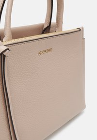 Sac à main en cuir beige avec finition texturée, équipé d'une fermeture éclair dorée et d'un logo de marque. Comprend des poignées doubles et une forme structurée.