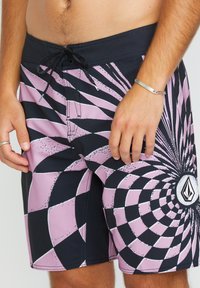 Costume da bagno neri e rosa con un motivo a scacchi spirale, dotati di una texture a rete e una vita con coulisse. Logo del marchio sul davanti.