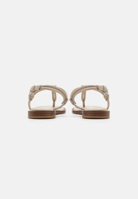 Sandales en cuir beige avec une semelle en bois plate et une sangle ajustable. Le design épuré présente des détails subtils et une texture lisse.