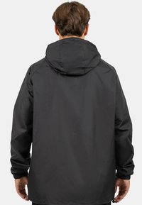 Zwarte waterdichte jas met een capuchon, elastische manchetten en een losse pasvorm. Soepele textuur, eenvoudig ontwerp en geen zichtbare logo's of patronen.