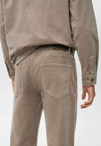 Pantalones de pana beige con un corte ajustado, que cuentan con dos bolsillos traseros, costuras sutiles y una textura suave.