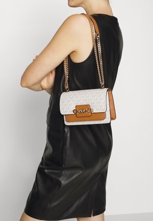 Femme portant une robe sans manches en cuir noir et un sac à bandoulière Michael Kors blanc et beige avec chaîne.