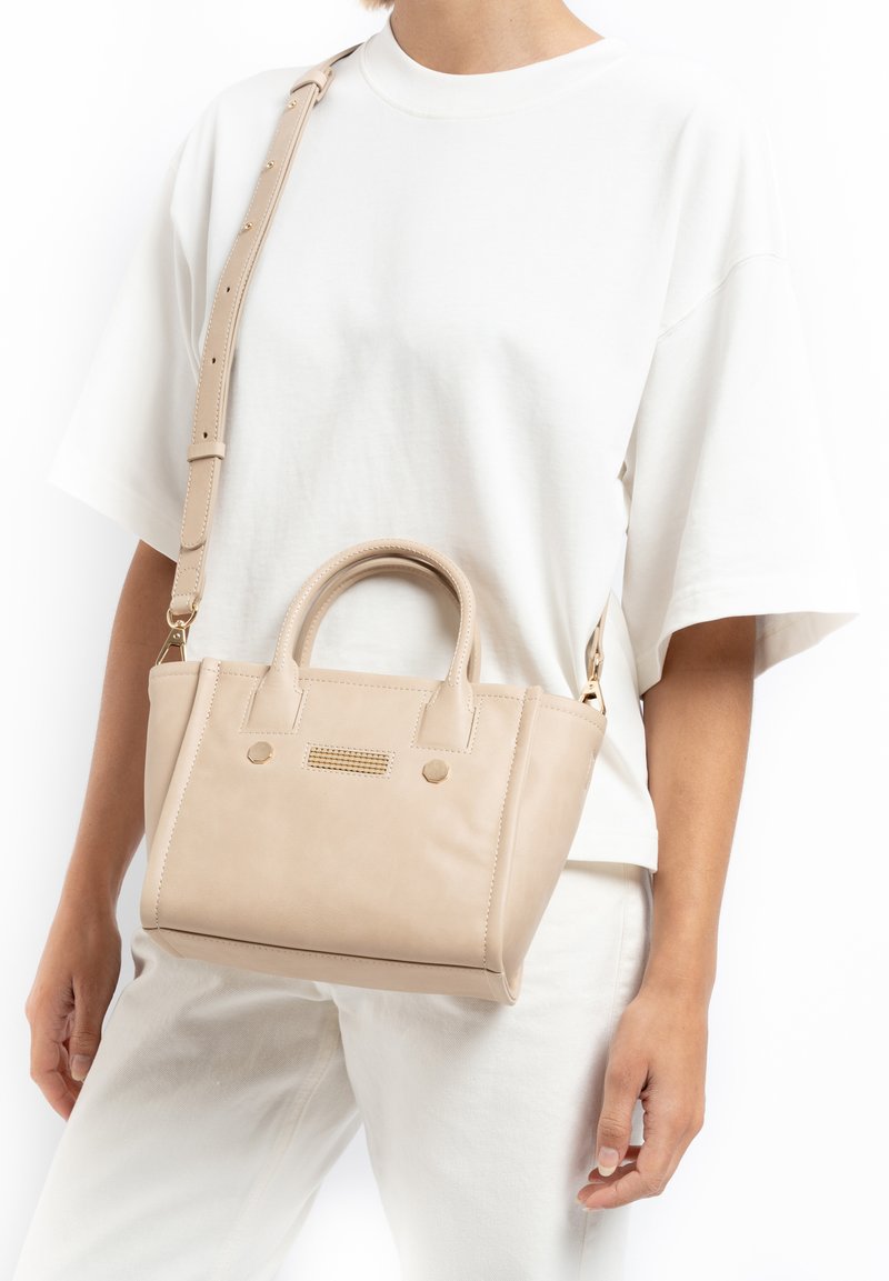 Beige leren handtas met korte handvatten, een afneembare schouderriem en een geprofileerde voorkant met kleine gouden accenten.