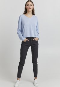 Lichtblauwe, getextureerde, lange mouwen trui met een V-hals. Gecombineerd met zwarte, slim-fit broek en witte sneakers.