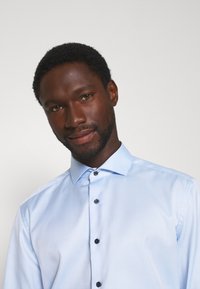 Lichtblauw overhemd gemaakt van gladde stof, met een klassieke kraag, zwarte knopen en een slimfit ontwerp. Minimalistische stijl zonder patronen.