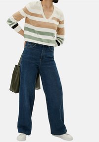 Pull rayé beige, vert et blanc avec un col en V, assorti à un jean bleu taille haute et large, ainsi qu'à des baskets blanches. Sac fourre-tout vert.