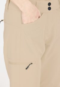 Beige cargobyxor med en mjuk textur, som har en sidoficka med dragkedja, framfickor och två svarta knappar i midjan.