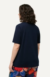 Camiseta de manga corta azul marino con cuello redondo y un corte relajado, combinada con pantalones de estampado floral colorido. Textura de tela suave.