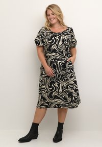 Schwarzes und cremefarbenes marmoriertes Kleid mit kurzen Puffärmeln, einem taillierten Gürtel und Taschen; kombiniert mit schwarzen Knöchelstiefeln.