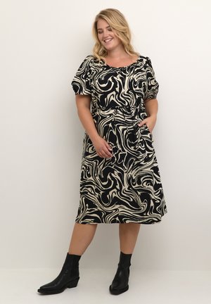 Schwarzes und cremefarbenes marmoriertes Kleid mit kurzen Puffärmeln, einem taillierten Gürtel und Taschen; kombiniert mit schwarzen Knöchelstiefeln.